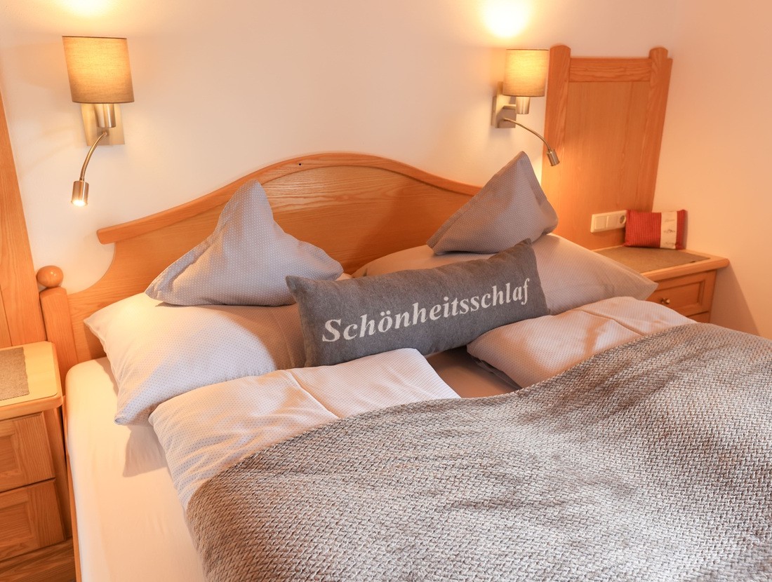 Gemütliches Bett mit Kissen, eines mit "Schönheitsschlaf" beschriftet