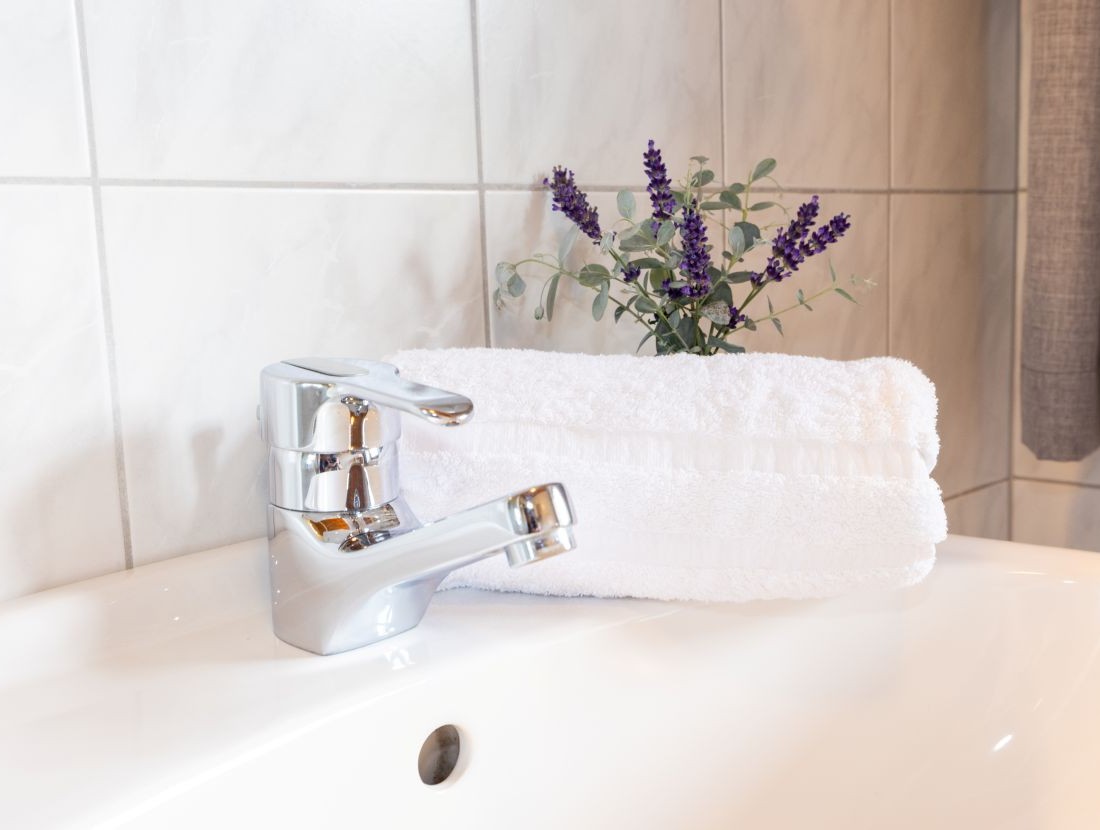 Ein Wasserhahn neben einem weißen Handtuch und Lavendel auf einem Waschbecken
