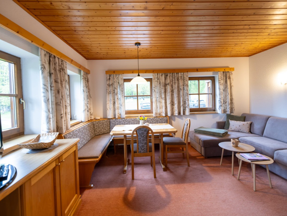Gemütliches Wohnzimmer mit Holztisch, Eckbank, Sofa und großem Fenster mit Vorhängen