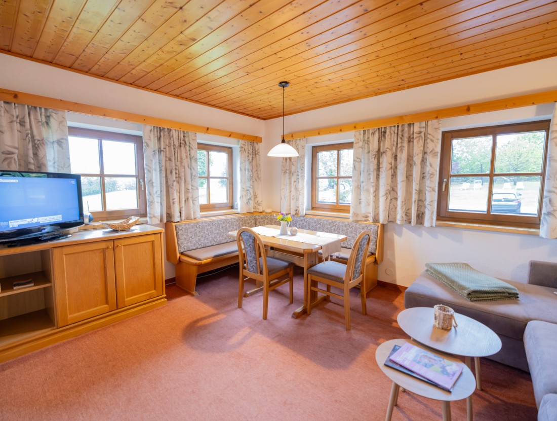 Helles Wohnzimmer mit Holzmöbeln, Eckbank und Fenstern, die Tageslicht hereinlassen