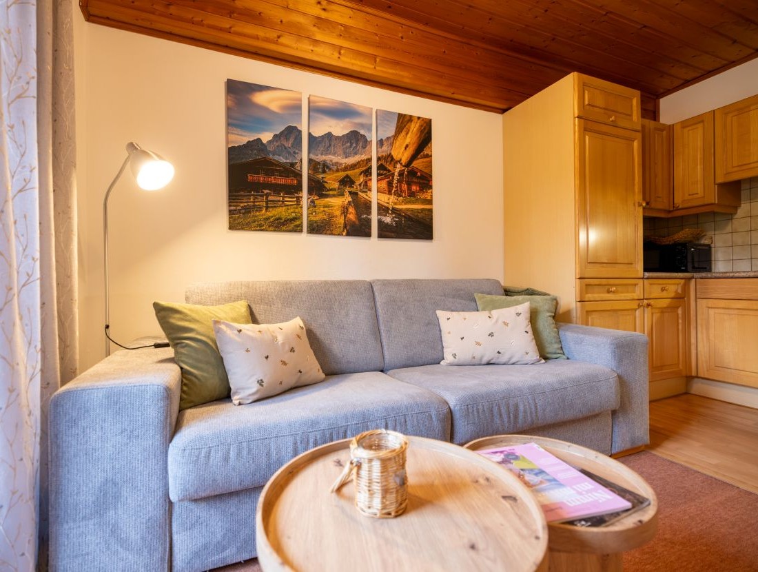 Gemütliches Wohnzimmer mit grauem Sofa, Holztisch und Bergbild an der Wand