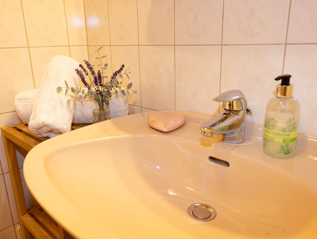 Waschbecken mit Seife, Handtüchern und einer Vase mit Lavendel auf einem Regal