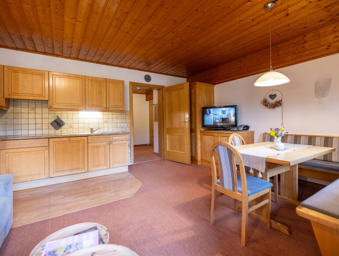 Gemütliches Wohnzimmer mit Holzküche, Esstisch und Fernseher im Landhausstil