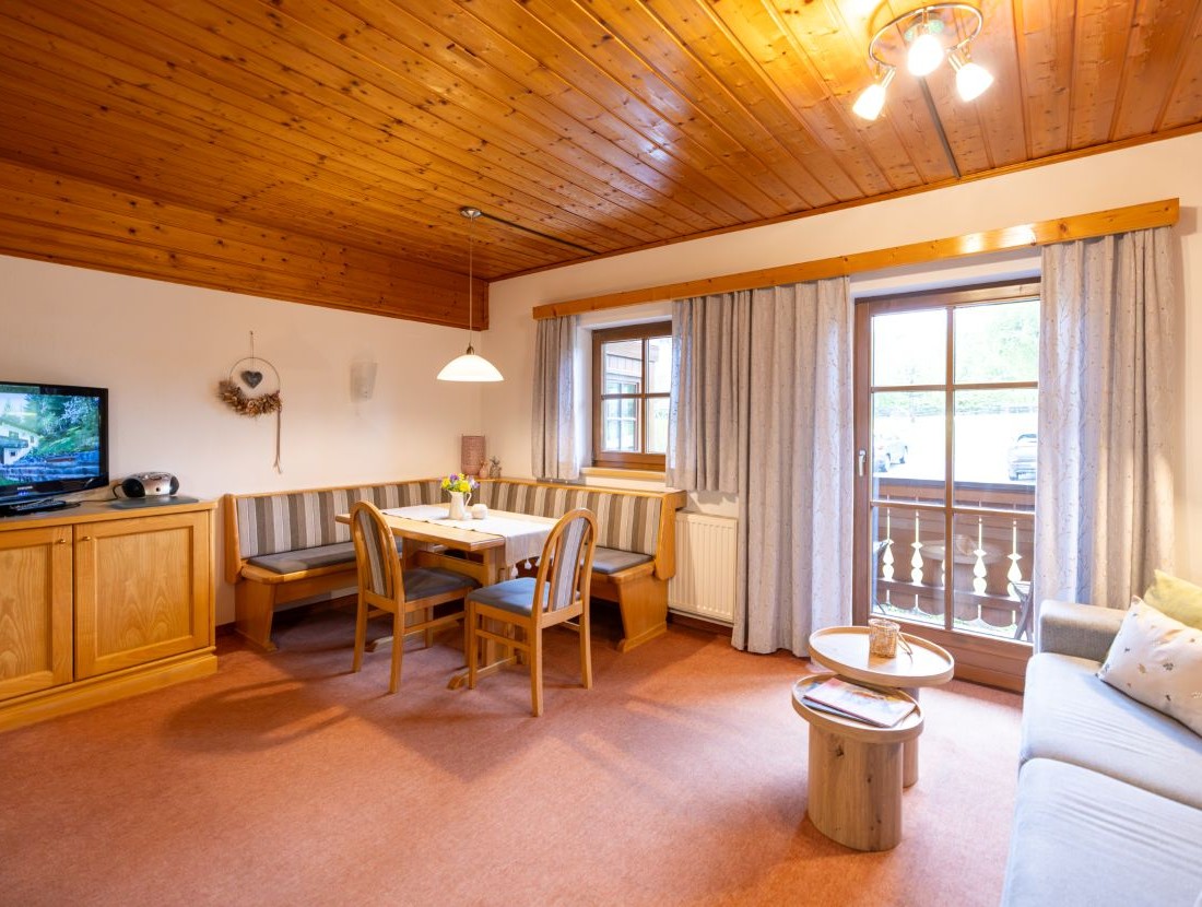 Gemütliches Wohnzimmer mit Holzmöbeln, Sofa, Esstisch und Fenstertür zum Balkon
