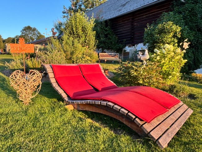 Rote Liege im Garten neben dekorativem Herz und Holzhaus im Hintergrund