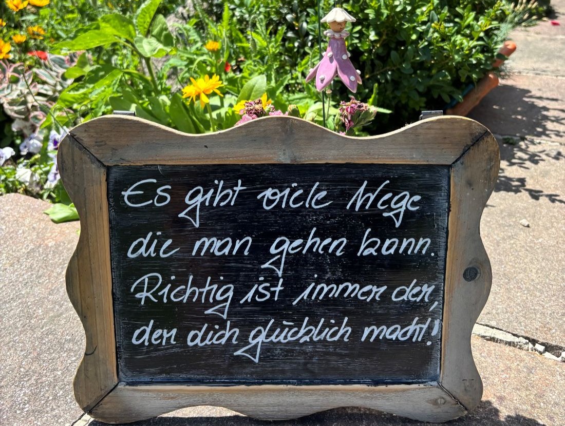 Kleines Holzschild im Garten mit motivierendem Spruch, umgeben von bunten Blumen